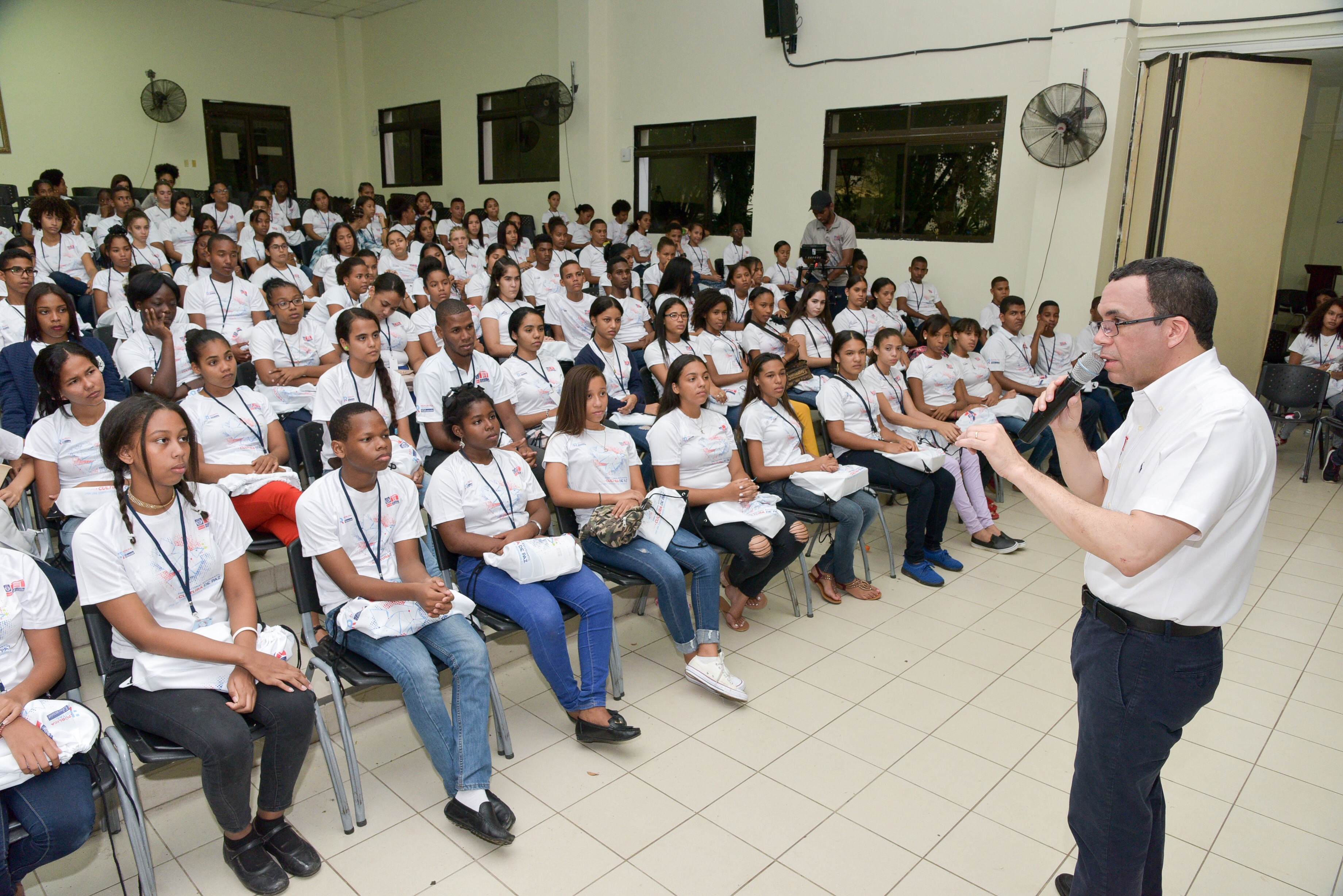  imagen Ministro Andr&eacute;s Navarro de pie expone con microfono frete a estudiantes participantes del Foro Nacional Estudiantil los cuales se encuentran sentados escuchando atentamente. 