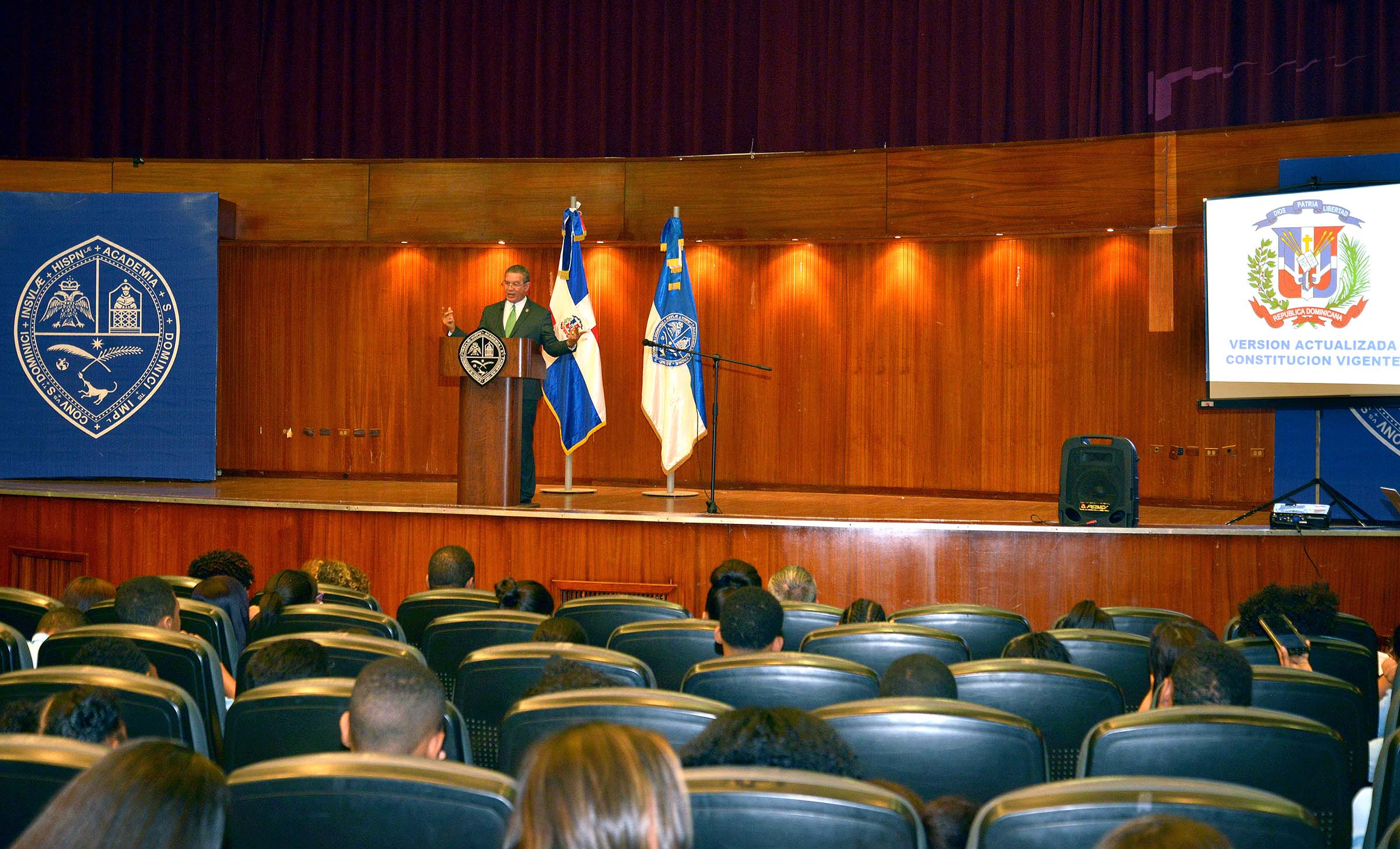  imagen Conferencista de pie en podium se dirife a estudiantes sentados 