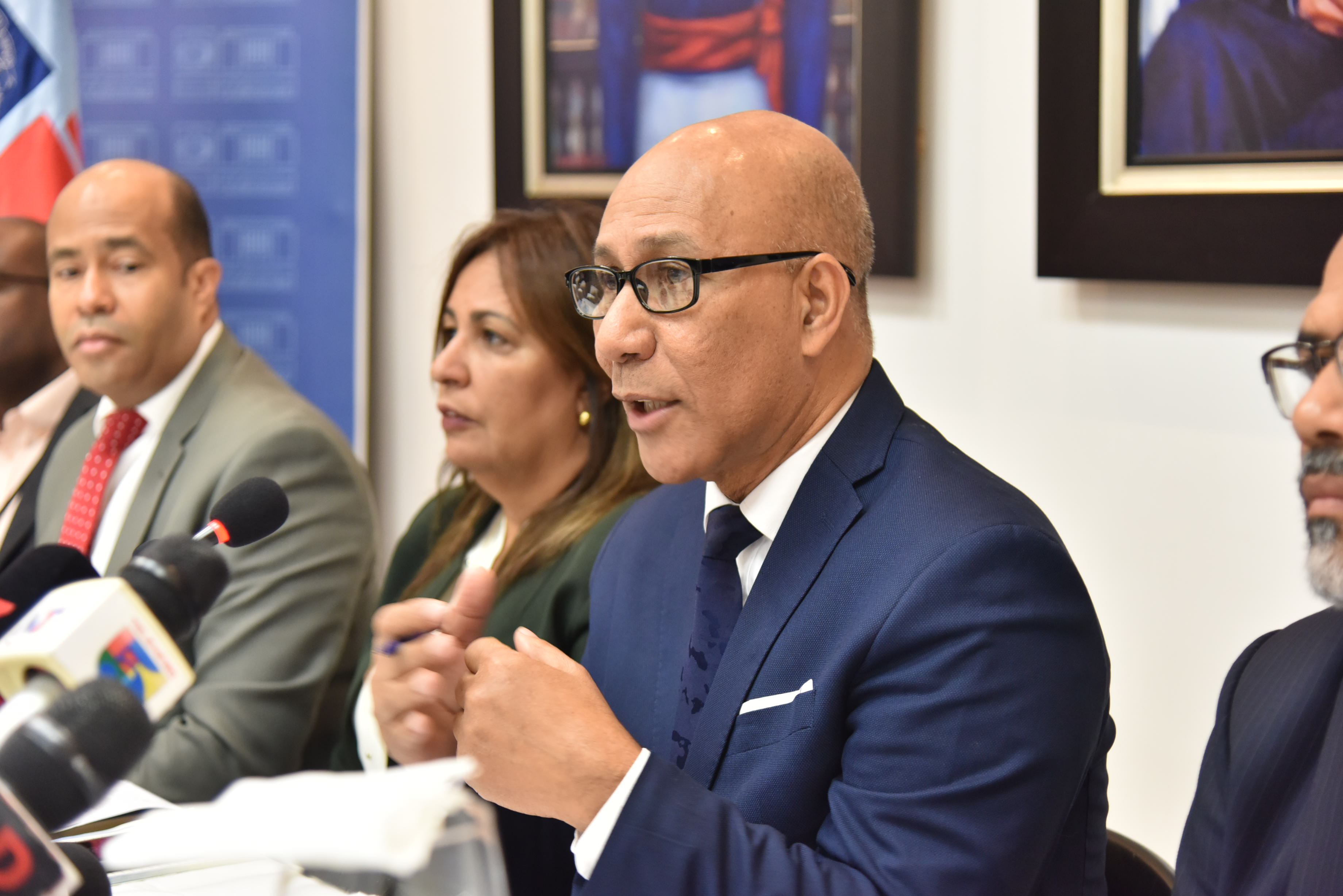  imagen Henry Santos junto a otras personalidades, sentados frente a la prensa durante rueda de prensa. 